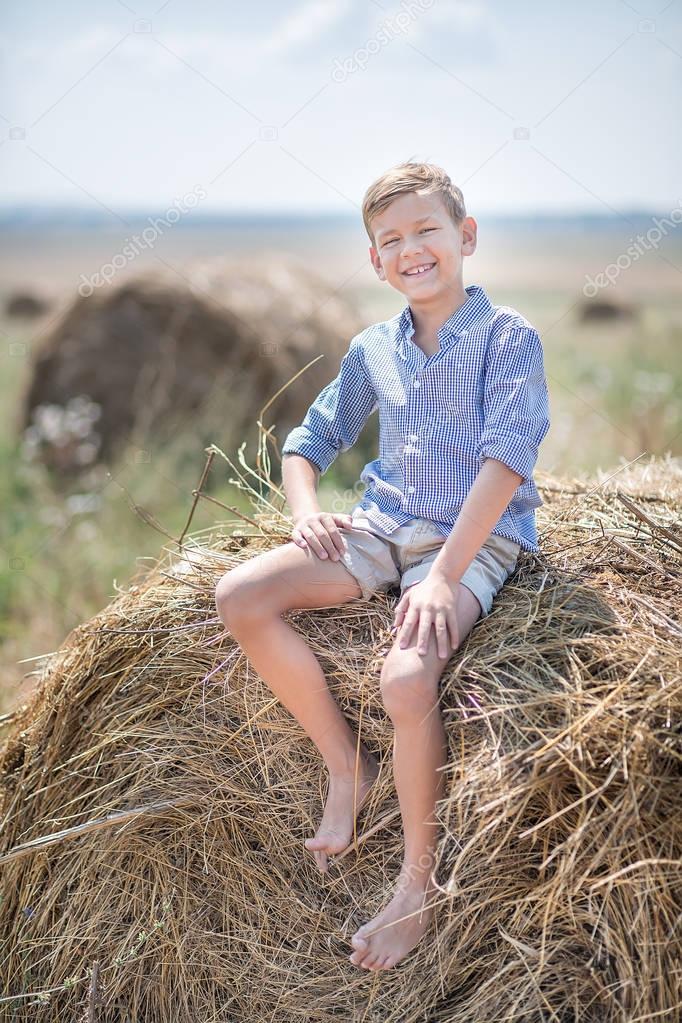 Attractive boy sitting on a haystack and smiling