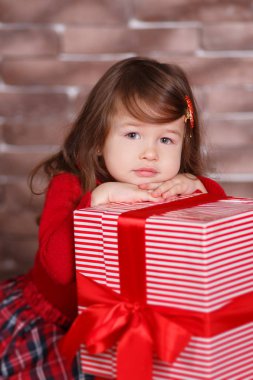 Kırmızı kazak kazak chequers onay ekose etek kayış ayakkabı pout dudak ve pembe yanakları ile büyük hediye ile stüdyo kış oturan poz gülümseyen genç esmer dolly Bayan kız şık giyinmiş.