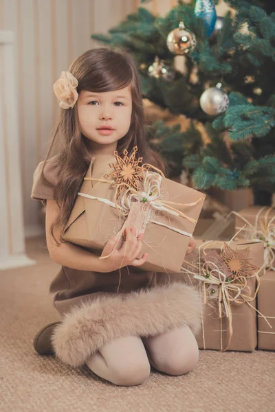 Νέοι μελαχρινή κουκλίτσα κυρία κορίτσι κομψά ντυμένος άνετα ζεστό χειμώνα γκρι μπουφάν με γούνα θέτοντας συνεδρίαση στέκεται στο studio κοντά στο δέντρο Χριστούγεννα Πρωτοχρονιά και παρουσιάζει. — Φωτογραφία Αρχείου
