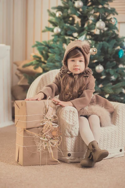 Joven morena muñeca dama chica elegante vestido acogedor abrigado invierno gris chaqueta con piel posando sentado en el estudio cerca de árbol de Año Nuevo de Navidad y regalos . — Foto de Stock