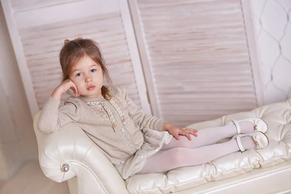 Young brunette dolly lady girl stylish dressed in white skirt midi petticoat and cardigan strap shoes smiling posing sitting in studio on old style sofa couch divan with pout lips and pink cheeks. — Stock Photo, Image