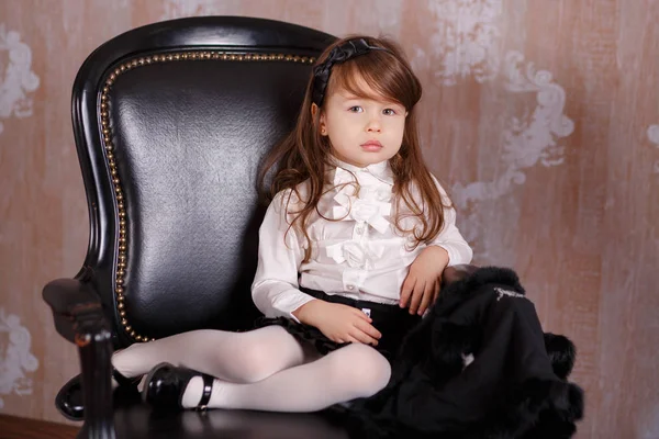 Unga brunett dolly lady tjej elegant klädd som en boss i vit officiella skjorta svart kjol poserar sittande i studio på svart läder stol med Skäggtorsk läppar och rosa kinder. — Stockfoto