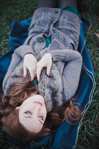 Sensual dama morena con los labios rosados y las mejillas blancas con suéter acogedor casual con piel posando sentarse sobre hierba verde en el bosque de otoño parque central — Foto de Stock