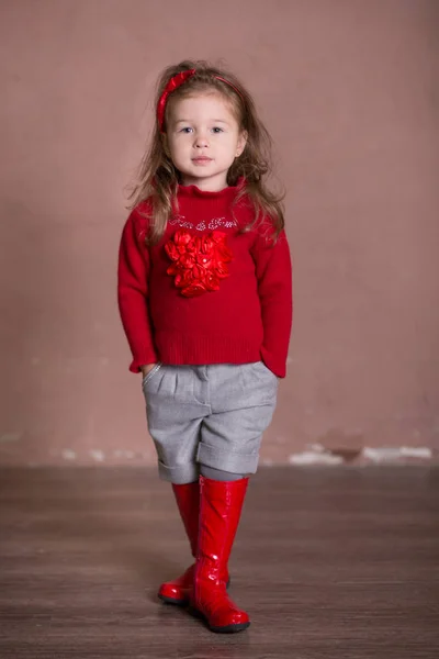 Pretty girl with brunnete hair stylish dressed in red sweater pullover warm winter shorts pants happyly smiling posing to camera for photosession in modern showroom studio wearing baby boots. — Stock Photo, Image