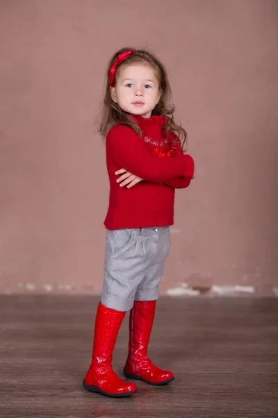 Pretty girl with brunnete hair stylish dressed in red sweater pullover warm winter shorts pants happyly smiling posing to camera for photosession in modern showroom studio wearing baby boots. — Stock Photo, Image