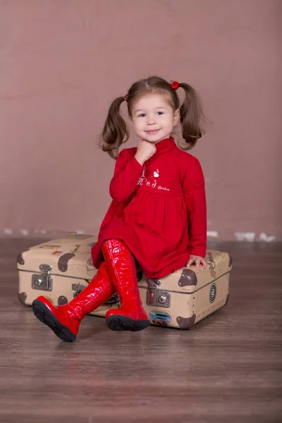 Pretty girl with brunnete hair stylish dressed red long shirt dress with cornrow happyly smiling posing camera photosession modern showroom studio wearing baby boots sitting standing travelling trunk. — Stock Photo, Image