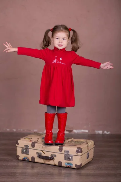 Pretty girl with brunnete hair stylish dressed red long shirt dress with cornrow happyly smiling posing camera photosession modern showroom studio wearing baby boots sitting standing travelling trunk. — Stock Photo, Image