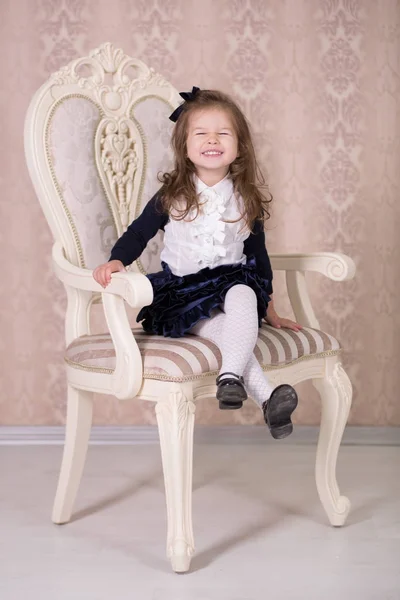 Pretty girl with brunnete hair and pout lips stylish dressed in old style shirt dress skirt posing to camera photosession in baroque showroom studio sitting on vertu virtu chair. — Stock Photo, Image