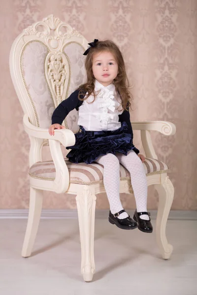 Pretty girl with brunnete hair and pout lips stylish dressed in old style shirt dress skirt posing to camera photosession in baroque showroom studio sitting on vertu virtu chair. — Stock Photo, Image