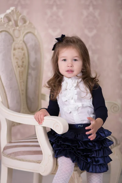 Pretty girl with brunnete hair and pout lips stylish dressed in old style shirt dress skirt posing to camera photosession in baroque showroom studio sitting on vertu virtu chair. — Stock Photo, Image