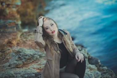 Romantik pout kırmızı dudaklar ve şık ceket giymiş pembe yanakları ile baştan çıkarıcı seksi Bayan kız elbise ve şort ile sonbahar bot ile kayalık plaj deniz tarafında poz telafi yüzünde ben romantik bölüm