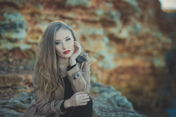 Seductora chica sexy con románticos labios rojos y mejillas meñique usando elegante vestido de chaqueta y pantalones cortos con botas de otoño posando en la playa rocosa junto al mar con maquillaje en la cara i episodio romántico — Foto de Stock