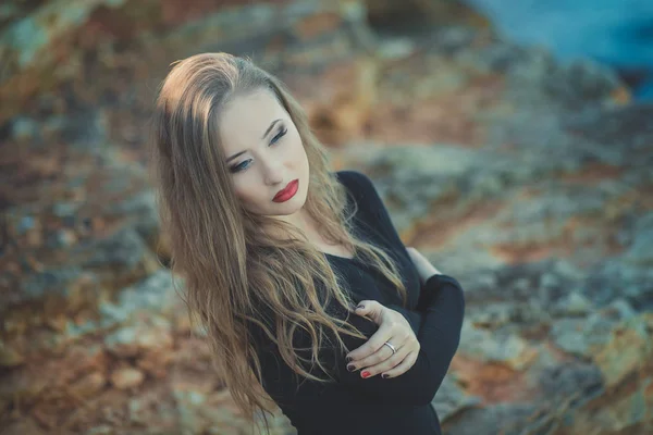 Seductora chica sexy con románticos labios rojos y mejillas meñique usando elegante vestido de chaqueta y pantalones cortos con botas de otoño posando en la playa rocosa junto al mar con maquillaje en la cara i episodio romántico — Foto de Stock