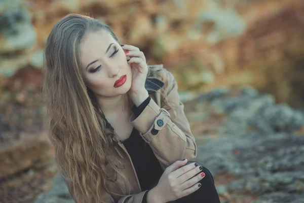 Seductora chica sexy con románticos labios rojos y mejillas meñique usando elegante vestido de chaqueta y pantalones cortos con botas de otoño posando en la playa rocosa junto al mar con maquillaje en la cara i episodio romántico — Foto de Stock