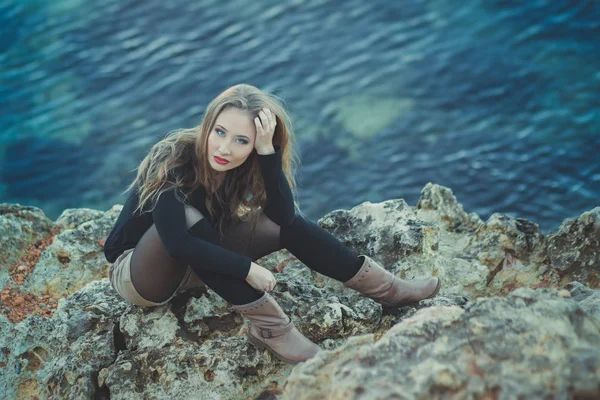 Seductora chica sexy con románticos labios rojos y mejillas meñique usando elegante vestido de chaqueta y pantalones cortos con botas de otoño posando en la playa rocosa junto al mar con maquillaje en la cara i episodio romántico — Foto de Stock