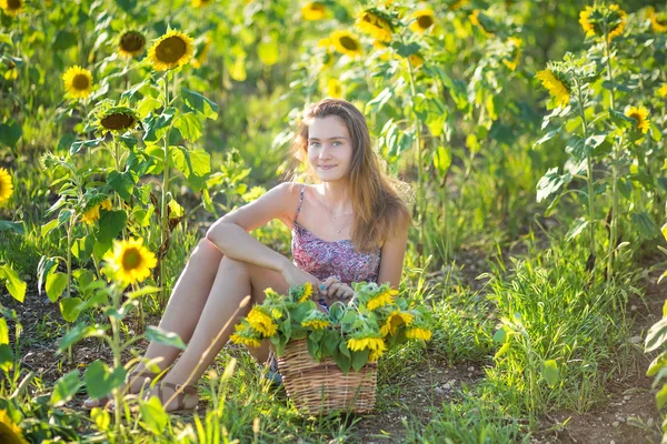 Mignon belle jeune fille dame femme assise sur un champ avec de grands tournesols. Brunette avec des yeux bleus portant robe colorée chapeau chapeau de chapeau de soleil leghorn italien sur dale lea de fleurs jaunes vertes fleur . — Photo