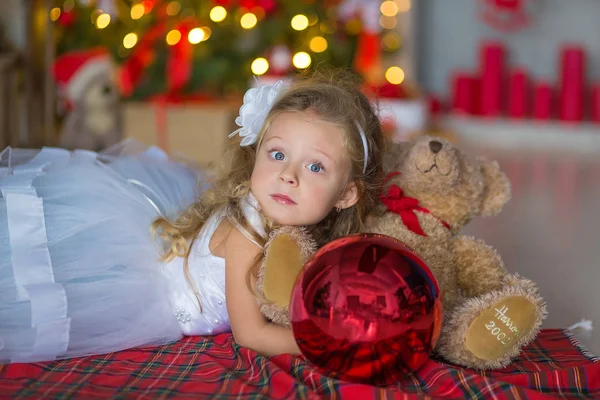 Mooie meisje in blauw wit elegante avondjurk zittend op de vloer in de buurt van de kerstboom en cadeautjes op een new year eve. Interieur met kerstversiering. Ondiepe Dof en bokeh achtergrond — Stockfoto