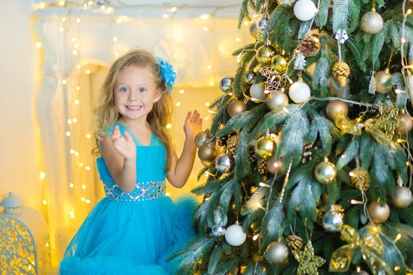 Junge schöne Mädchen in blau weiß eleganten Abendkleid sitzt auf dem Boden in der Nähe von Weihnachtsbaum und Geschenke an einem Silvesterabend. Interieur mit Weihnachtsdekoration. flacher Dof und Bokeh-Hintergrund — Stockfoto