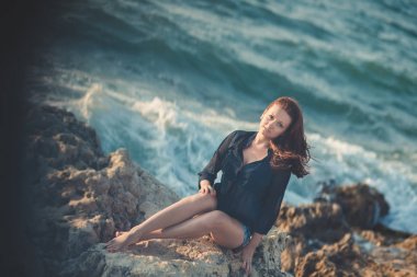 Sıcak seksi şık giyimli genç bayan esmer kılları ve pembe yanakları açık bacaklar omuz ve kolları duygusallık deniz tarafı kayalık sahilde poz ile. baştan çıkarıcı kadın gelecekteki denizci kocası bekliyor