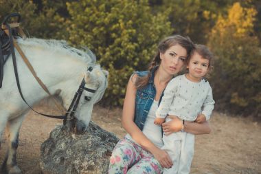 Romantik bir sahne güzel Bayan genç anne şirin bebek kızıyla birlikte zevk zaman birlikte şehir köy park yürüme beslenme beyaz at midilli içinde