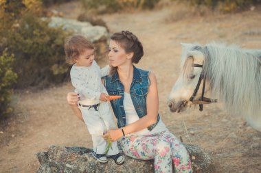 Romantik bir sahne güzel Bayan genç anne şirin bebek kızıyla birlikte zevk zaman birlikte şehir köy park yürüme beslenme beyaz at midilli içinde