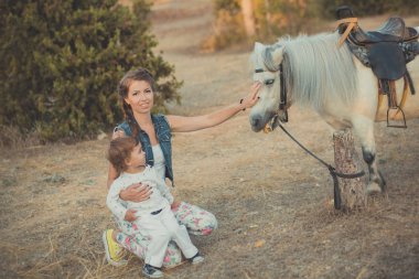Romantik bir sahne güzel Bayan genç anne şirin bebek kızıyla birlikte zevk zaman birlikte şehir köy park yürüme beslenme beyaz at midilli içinde