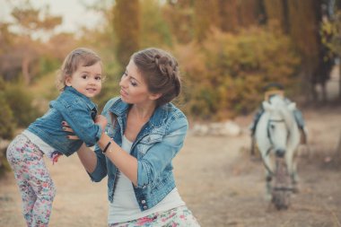Romantik bir sahne güzel Bayan genç anne şirin bebek kızıyla birlikte zevk zaman birlikte şehir köy park yürüme beslenme beyaz at midilli içinde