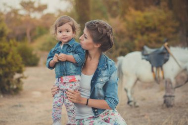 Romantik bir sahne güzel Bayan genç anne şirin bebek kızıyla birlikte zevk zaman birlikte şehir köy park yürüme beslenme beyaz at midilli içinde