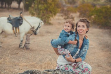 Romantik bir sahne güzel Bayan genç anne şirin bebek kızıyla birlikte zevk zaman birlikte şehir köy park yürüme beslenme beyaz at midilli içinde