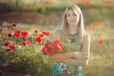 Sarışın adoreable hanımefendi kadın adoreable şehvetli gövdesi kırmızı çiçek haşhaş haşhaş ile buket ile deniz tarafı sahilde poz şık yaz renkli elbise