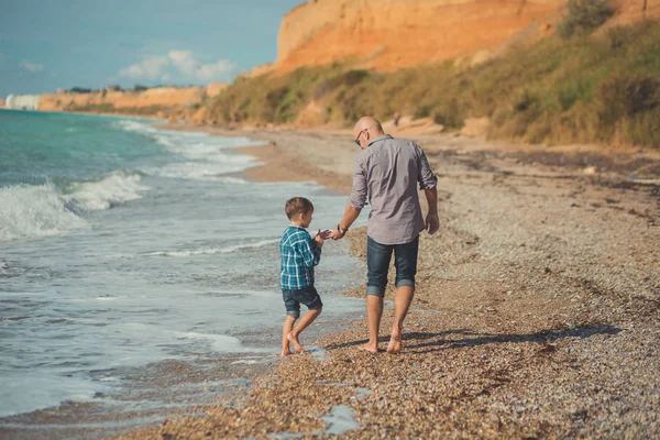 Sueño toque escena de padre guapo caminando en la playa de piedra lado del mar con lindo hijo con ropa elegante disfrutar de la hora de verano juntos — Foto de Stock