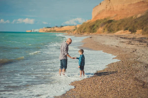 Sueño toque escena de padre guapo caminando en la playa de piedra lado del mar con lindo hijo con ropa elegante disfrutar de la hora de verano juntos — Foto de Stock