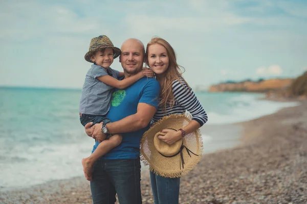 Hermosa escena increíble de la familia feliz del padre guapo hermosa señora madre y lindo niño pequeño posando juntos de mar playa de piedra del océano en vacaciones relajarse con ropa elegante — Foto de Stock