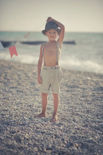 Милий старий хлопчик на пляжі ходить позуючи в вишуканих шортах з шибеницями та джентльменським капелюхом насолоджуйтесь літнім часом наодинці на чудовому океані з якорем. Чарівна сцена дитячого життя — стокове фото