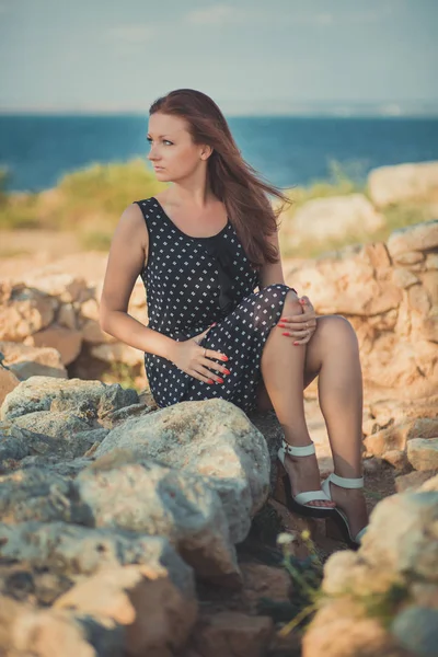 Caliente sexy elegante vestida joven morena pelos y mejillas rosadas con piernas abiertas hombros y brazos posando sensualidad en la playa rocosa lado del mar. seductora mujer esperando a su futuro marido marinero — Foto de Stock