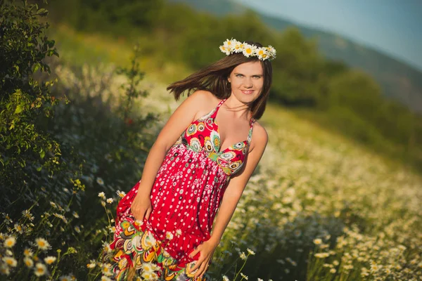 Charmante adorable jeune femme femme brune foncée poils et yeux verts tendre pose sexy avec des fleurs couronne sur le dessus de la tête et un énorme bouquet de camomille marguerite sauvage portant une robe élégante . — Photo