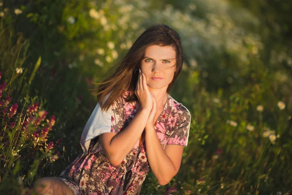 Charmante adorable jeune femme femme brune foncée poils et yeux verts tendre pose sexy avec des fleurs couronne sur le dessus de la tête et un énorme bouquet de camomille marguerite sauvage portant une robe élégante . — Photo