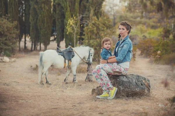 Scène romantique belle dame jeune mère avec son mignon bébé fille profiter du temps ensemble dans le parc du village de la ville marchant nourrir cheval blanc poney — Photo