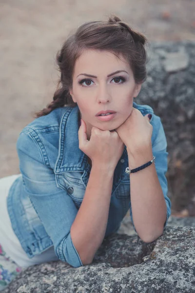 Enormes ojos marrones mujer joven posando en el parque central de piedra con pantalones vaqueros azules chaqueta blanca shirt.Brunette belleza con coleta y soportes en los dientes blancos brillantes — Foto de Stock