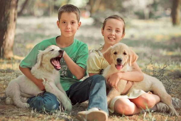 猎犬幼崽可爱的场景年轻的妹妹弟弟喜欢与最好的朋友狗象牙白色拉布拉多小狗的夏季时间度假。地无忧无虑的童年家庭生活世界梦想小狗. — 图库照片