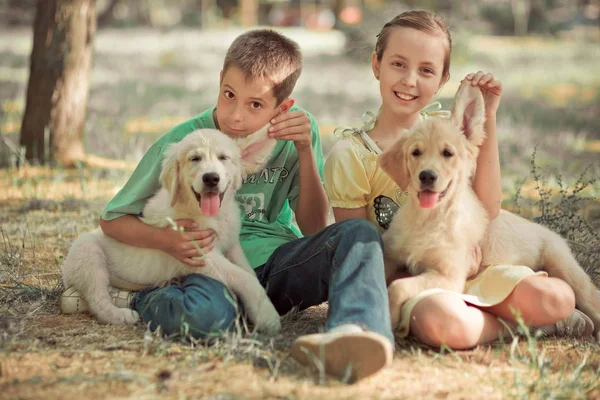 猎犬幼崽可爱的场景年轻的妹妹弟弟喜欢与最好的朋友狗象牙白色拉布拉多小狗的夏季时间度假。地无忧无虑的童年家庭生活世界梦想小狗. — 图库照片
