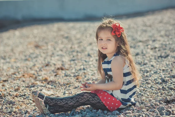 Schattig klein meisje genieten van zomertijd op zee kant strand gelukkig spelen met rode ster en tiny toy anker op zand draagt nobby kleren met donkerbruine haren — Stockfoto