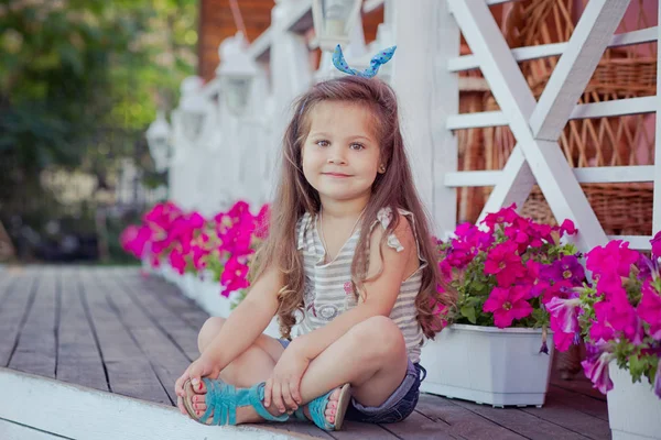 Elegante bella ragazza carina con capelli castani in posa su un giardino di legno pieno di fiori che indossano minuscole camicie jeans e ariosa vita bassa e sandali blu — Foto Stock