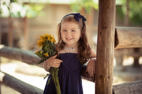 Giovane bambina con capelli castani e guance luminose pelle perfetta indossando elegante impressionante vestito blu in posa con mazzo di fiori gialli selvatici margherita — Foto Stock