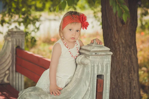 Retro stílusos felöltözve szőke fiatal baba lány gyermek pózol central park kerti visel francia couturer fehér ruha, piros-tarka selyemkendő és a virágfüzér — Stock Fotó