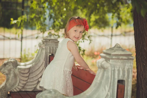 Retro stylish dressed blond young baby girl child posing in central park garden wearing french couturer white dress red bandana and chaplet — Stock Photo, Image