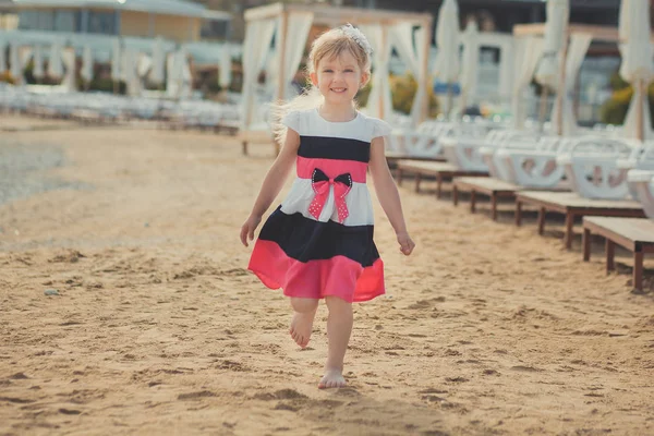 Young cute baby girl enjoying childhood summer time on sandy beach posing on wooden pier bridge wearing casual stylish dress — Stock Photo, Image
