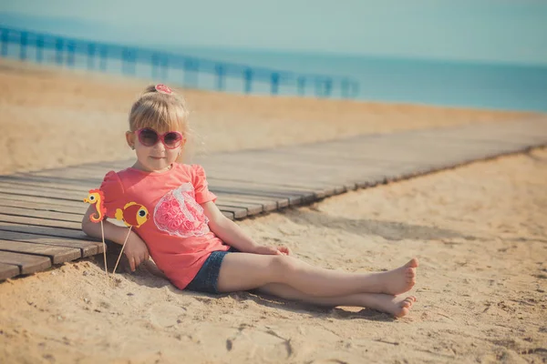 Jonge schattige babymeisje genieten van jeugd zomertijd aan zandstrand poseren op houten pier brug dragen casual stijlvolle kleding — Stockfoto