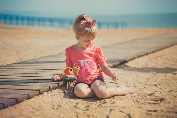 Giovane ragazza carina godendo infanzia estate tempo sulla spiaggia sabbiosa in posa sul ponte di legno molo indossando abito casual elegante — Foto Stock