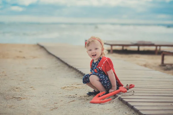 Schattig meisje met blond haar en roze apple Wang genieten van zomertijd vakantie poseren in prachtige strand vol met zand draagt stijlvolle jurk — Stockfoto